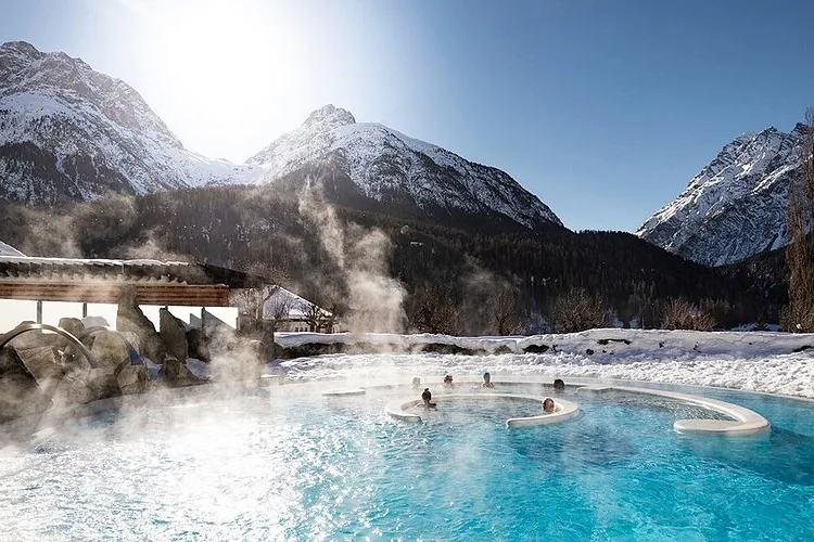 Het dampende buitenbad van Bogn Engiadina in Scuol, met besneeuwde bergen erachter.