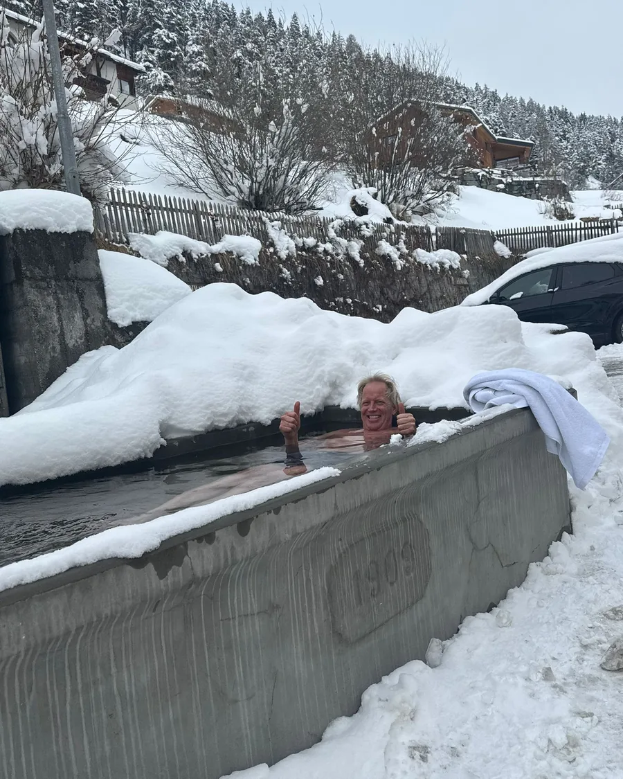 Iemand zit tot aan de schouders in het ijskoude water van de bron, tussen hoge sneeuwranden.